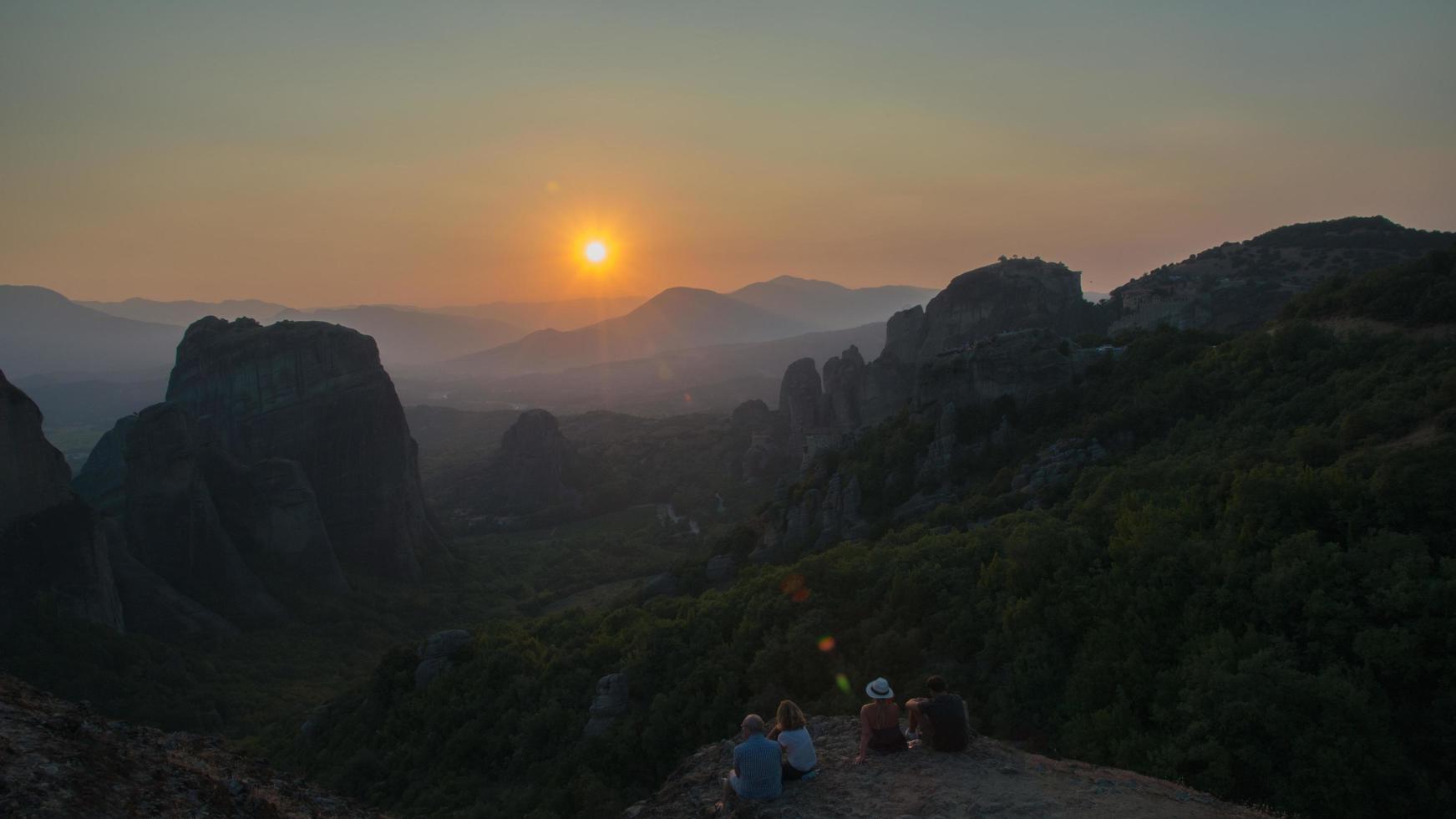 grupo de pessoas apreciando o pôr do sol nas montanhas de meteora, na Grécia foto