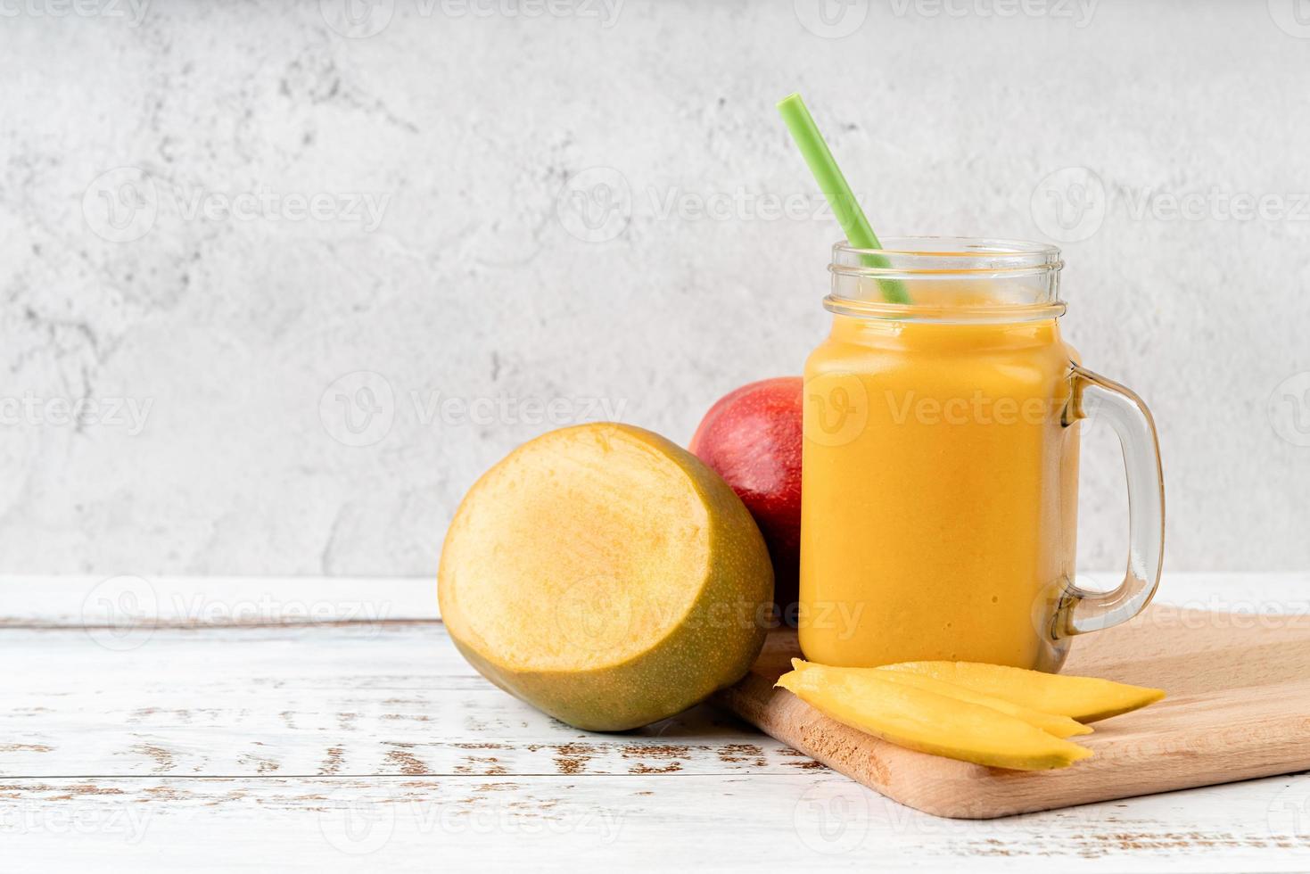 Smoothie de manga em um frasco de vidro decorado com fatias de manga, vista frontal em fundo de madeira foto