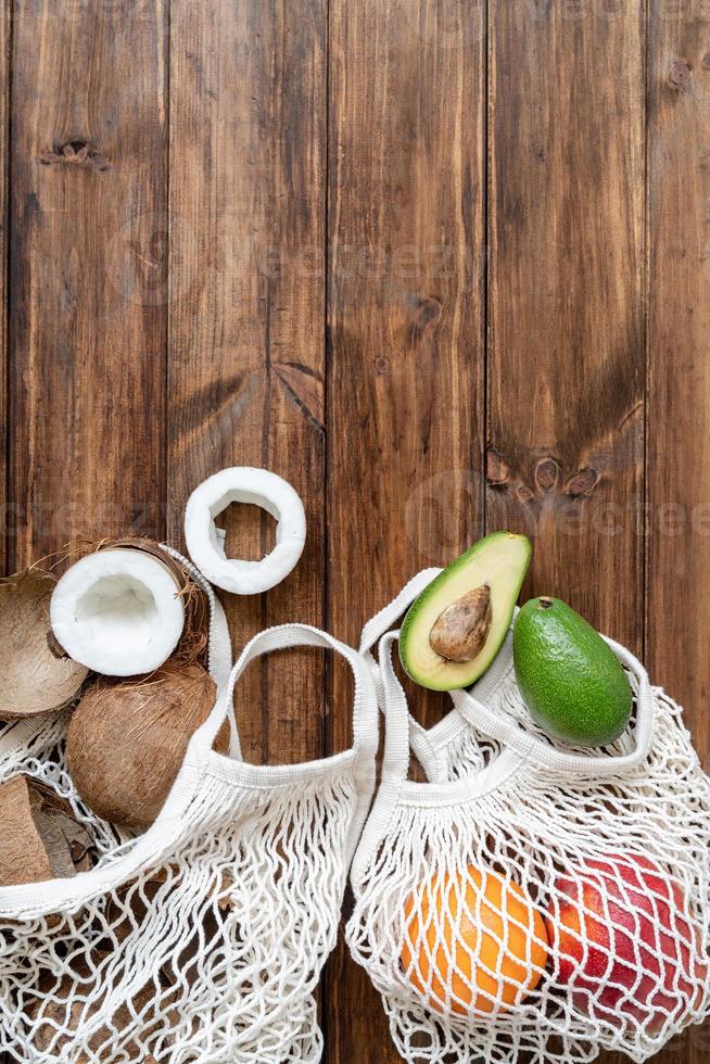 frutas tropicais frescas em uma bolsa de malha, vista superior plana, sobre fundo de madeira foto