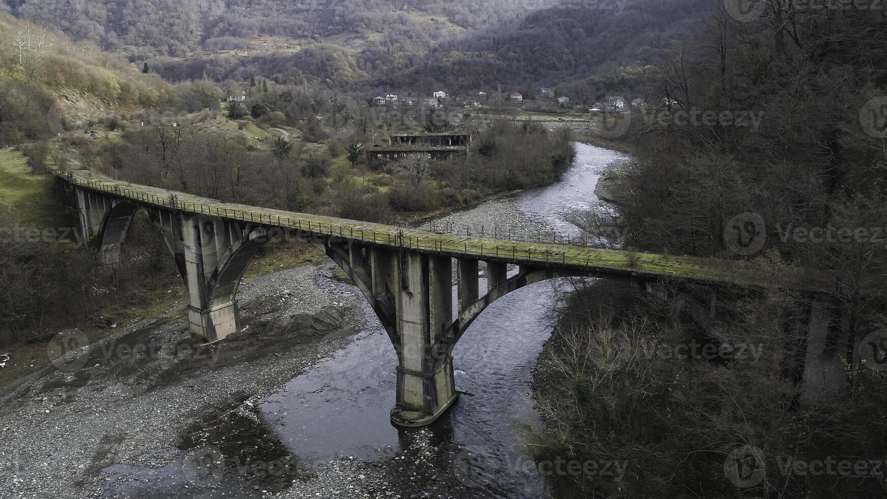 aéreo do abandonado concreto ponte coberto de musgo sobre a limitar rio. tomada. outono panorama com Alto arborizado montanhas e a pequeno Vila. foto