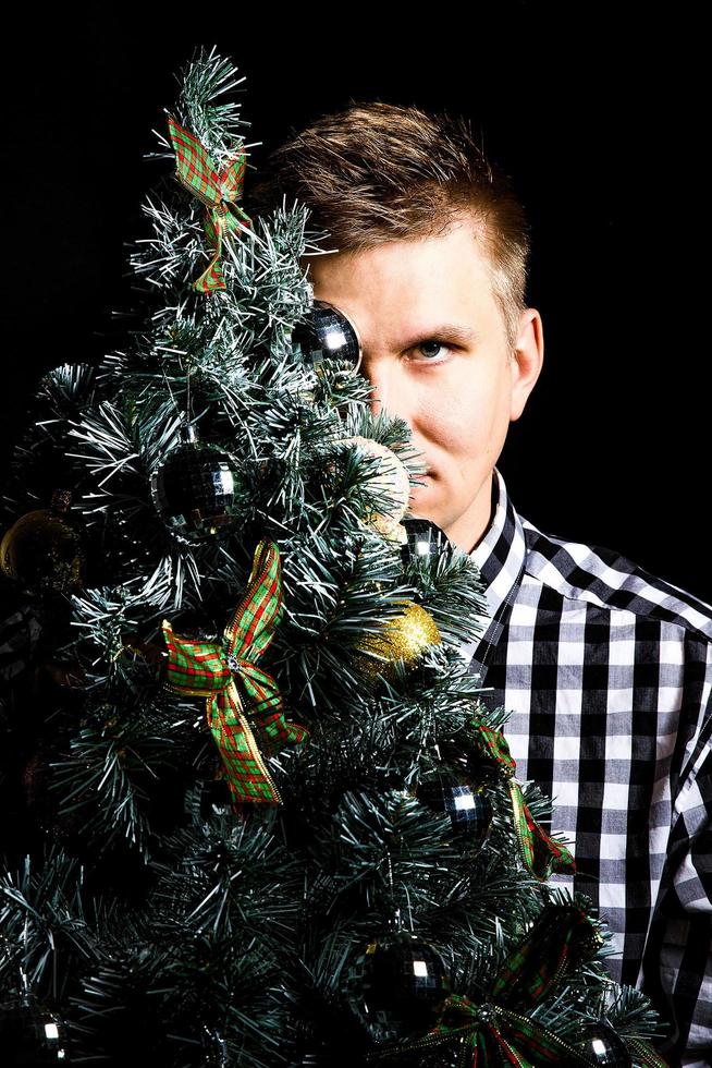 foto elegante de um homem escondendo o rosto atrás de uma árvore de Natal em um fundo preto. conceito de natal e ano novo