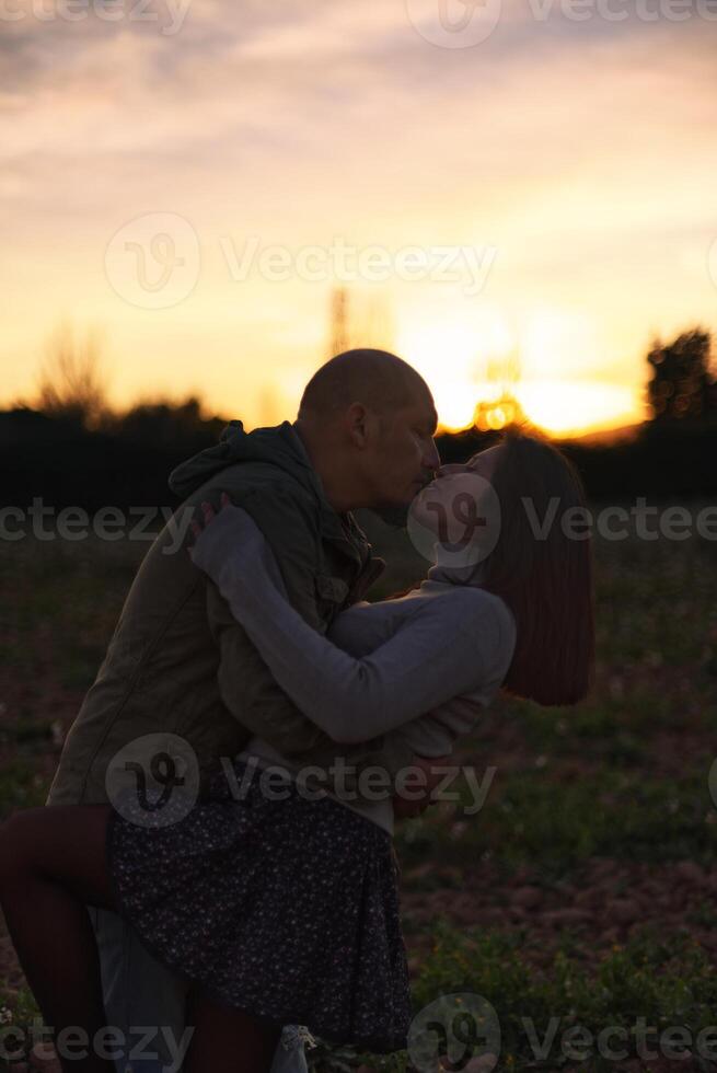 uma homem abraços e Beijos dele namorada às pôr do sol dentro uma natural ambiente. foto