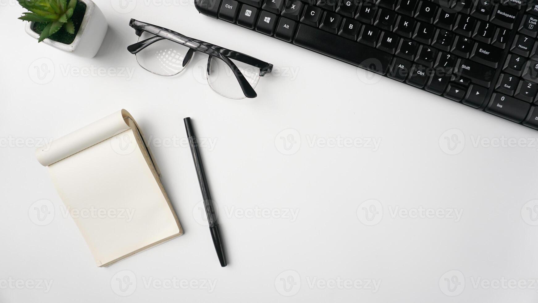 área de trabalho escrivaninha com cadernos, canetas, teclado, óculos e plantas em branco fundo foto
