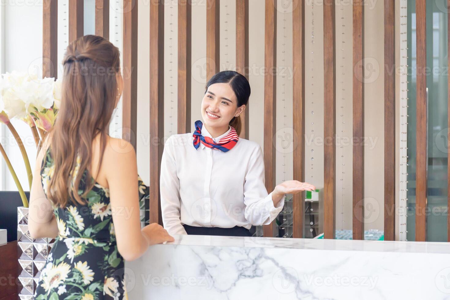 jovem ásia mulher recepcionista atrás a hotel contador atendendo para fêmea convidados. sorridente fêmea recepcionista trabalhando dentro uma hotel foto