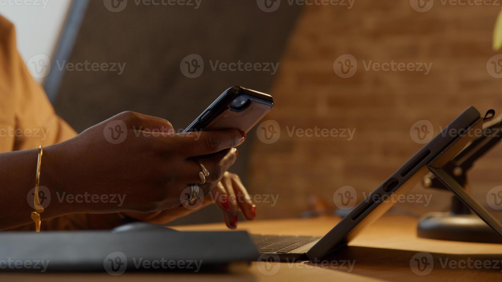 Feche as mãos de uma mulher negra madura na mesa, digitando no laptop e segurando o telefone enquanto fala foto