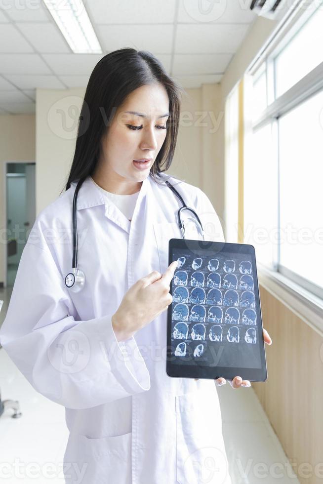 retrato de uma médica inteligente segurando o tablet para mostrar uma imagem de raio-x e em pé na recepção do hospital. foto