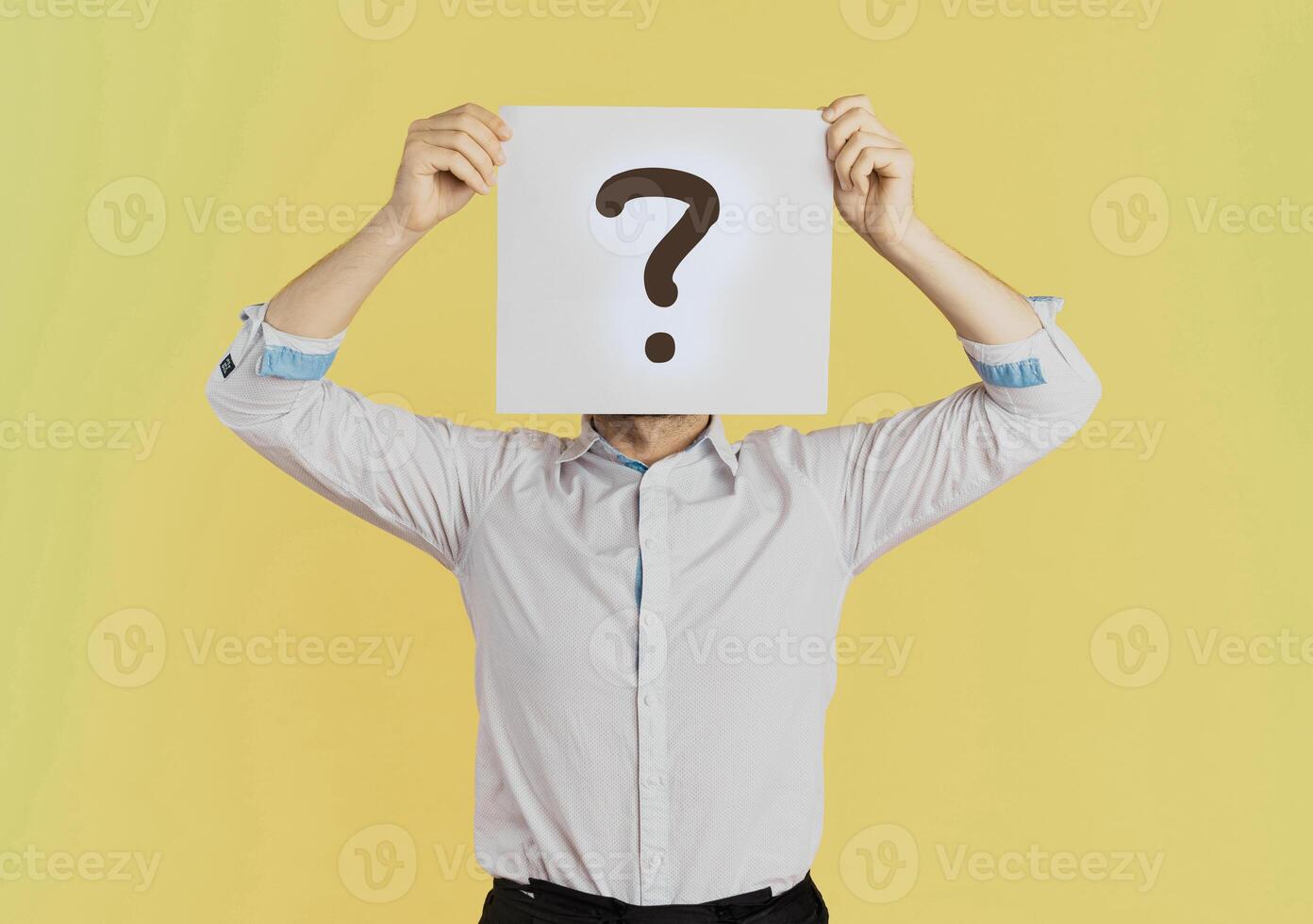 jovem homem de negocios cobertura face segurando papel com questão marca símbolo. em pé sobre isolado amarelo fundo foto