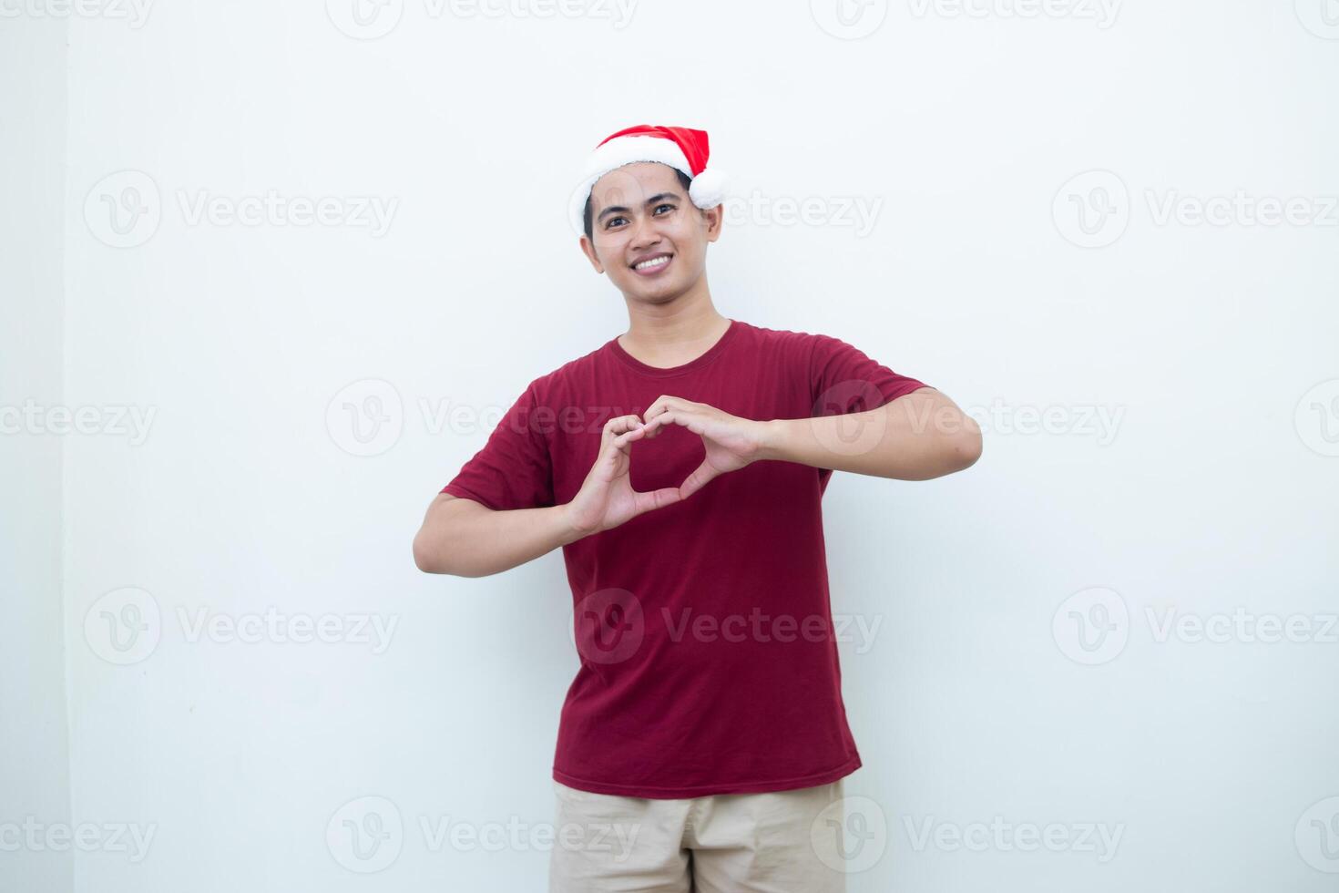 jovem ásia homem vestindo uma santa claus chapéu expressando amor de formando uma coração símbolo com dele mãos isolado de uma branco fundo para visual comunicação foto