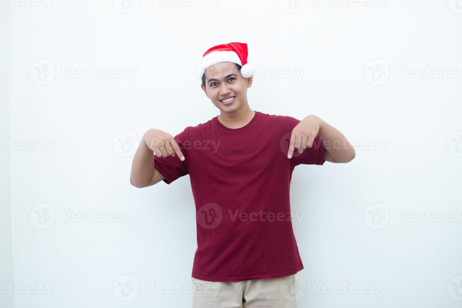 jovem ásia homem vestindo uma santa claus chapéu sorridente, choque e apontando para dela lado isolado de branco fundo para visual comunicação foto