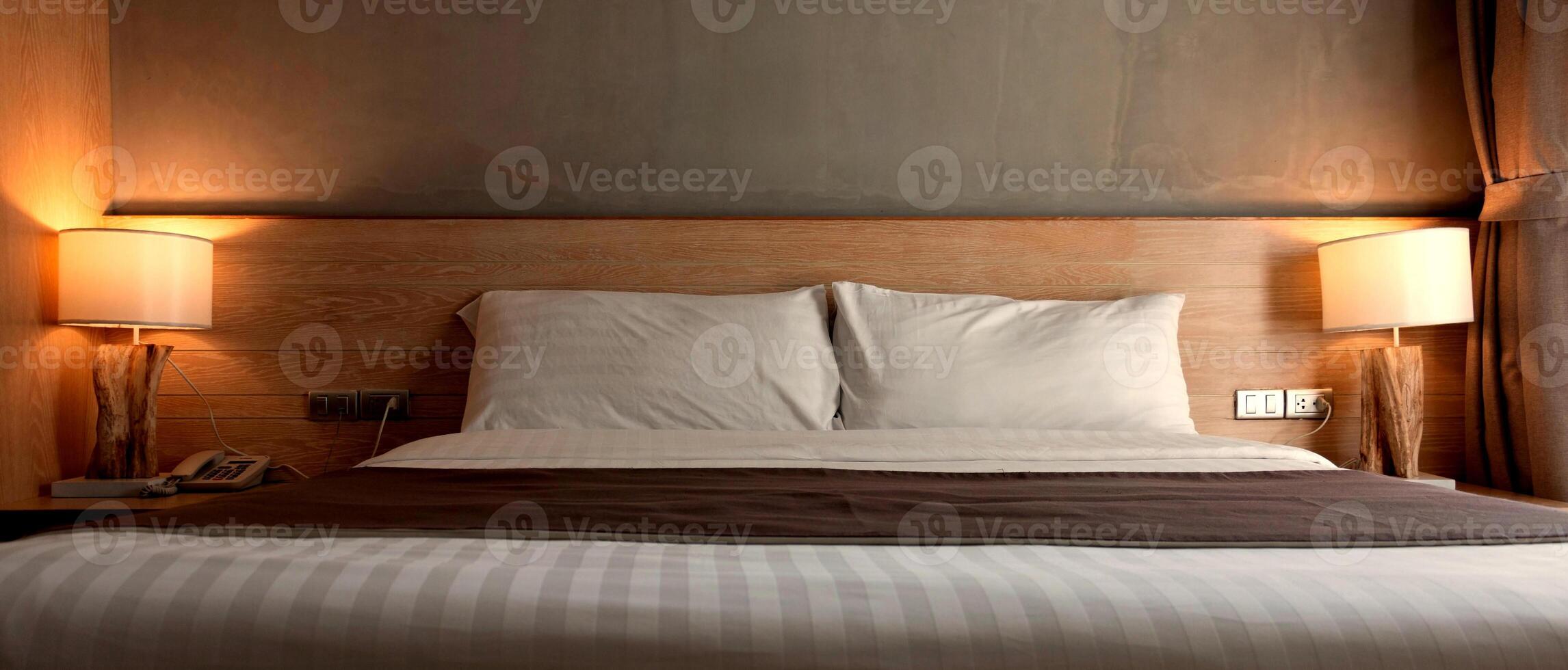 branco almofadas em cama com luminária luz às noite foto