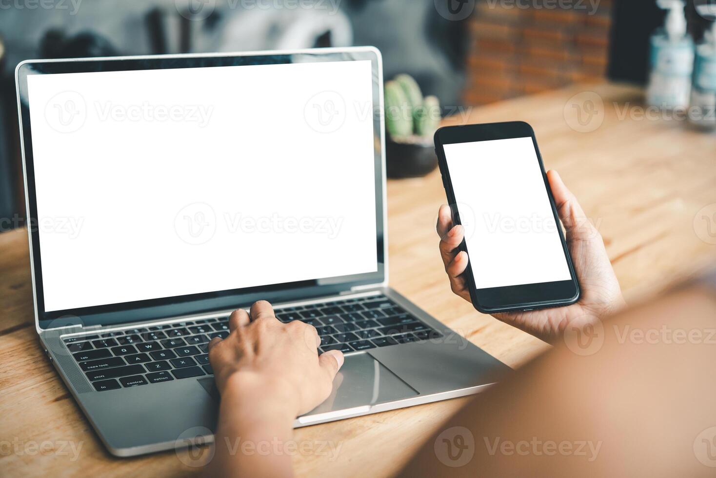 brincar imagem do uma mulher mão trabalhando em uma computador portátil e inteligente telefone com em branco branco Área de Trabalho cópia de espaço tela em uma escrivaninha foto