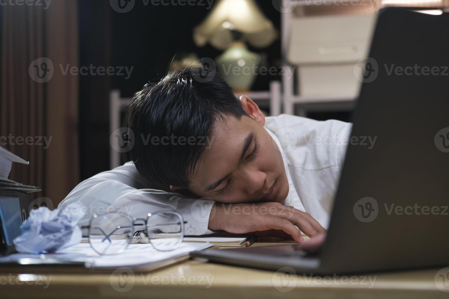 jovem cansado homem de negocios deitado em mesa às noite escritório. foto