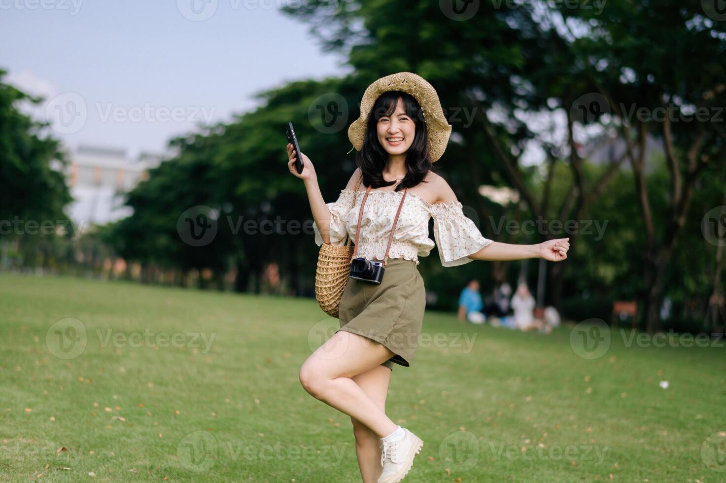 retrato do ásia jovem mulher viajante com tecelagem chapéu, cesta, Móvel telefone e Câmera em verde público parque fundo. viagem viagem estilo de vida, mundo viagem explorador ou Ásia verão turismo conceito. foto