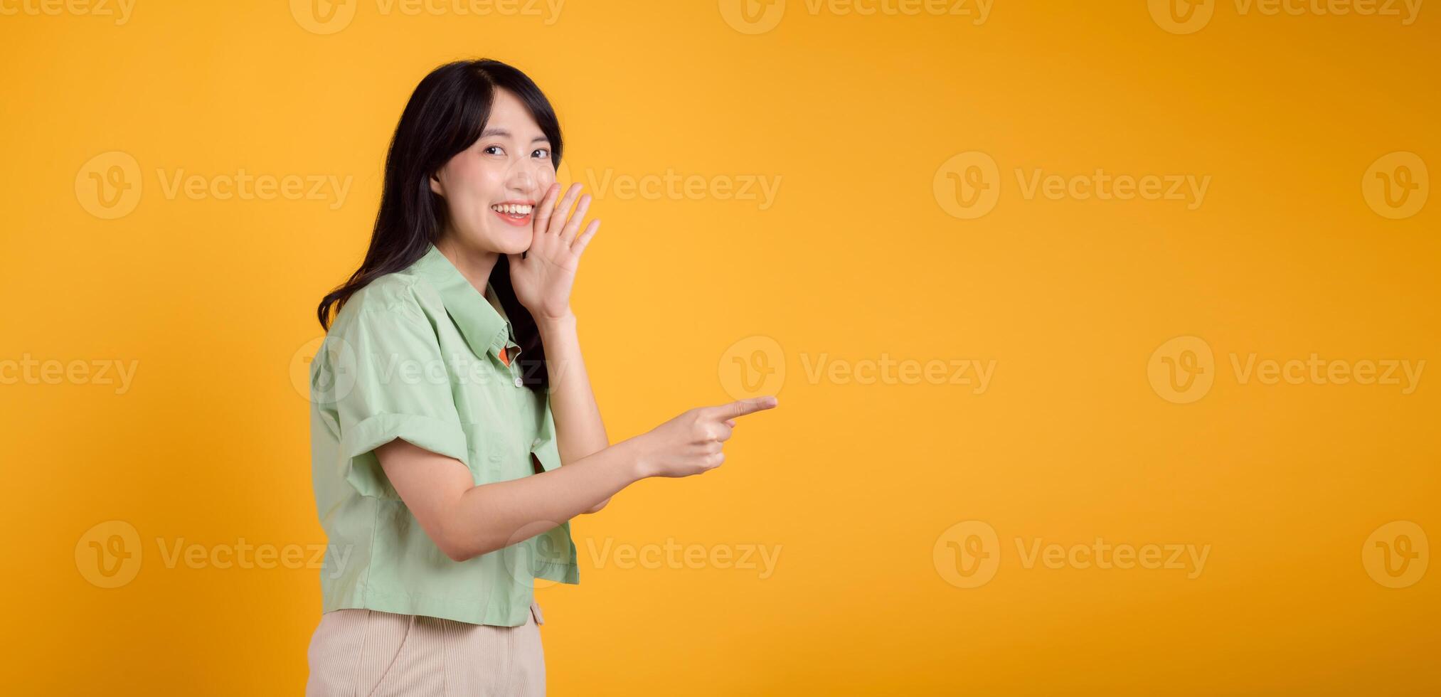 capturar noivado e excitação com ásia jovem mulher desgasta pastel verde camisa em laranja camisa mostrar feliz sorrir enquanto colocação mão sobre boca e apontando com uma dedo para livre cópia de espaço. foto