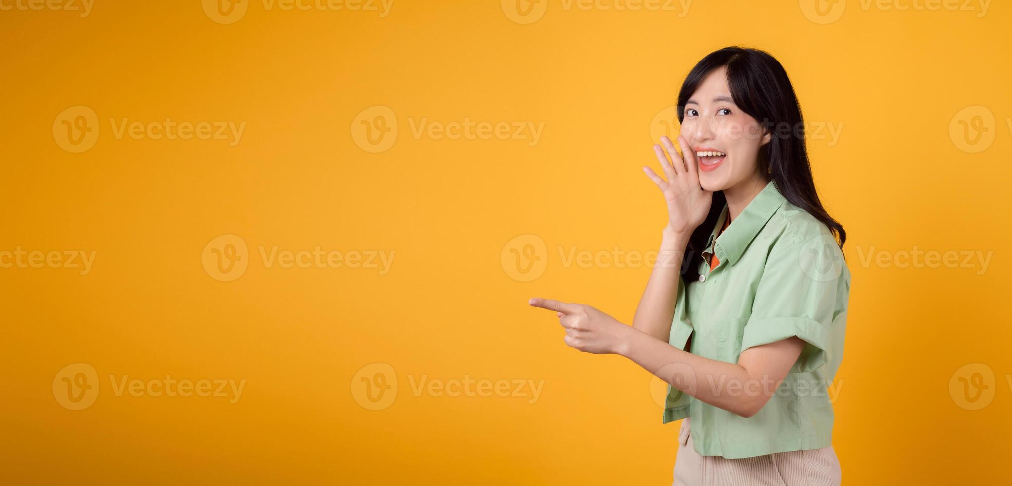 capturar noivado e excitação com ásia jovem mulher desgasta pastel verde camisa em laranja camisa mostrar feliz sorrir enquanto colocação mão sobre boca e apontando com uma dedo para livre cópia de espaço. foto