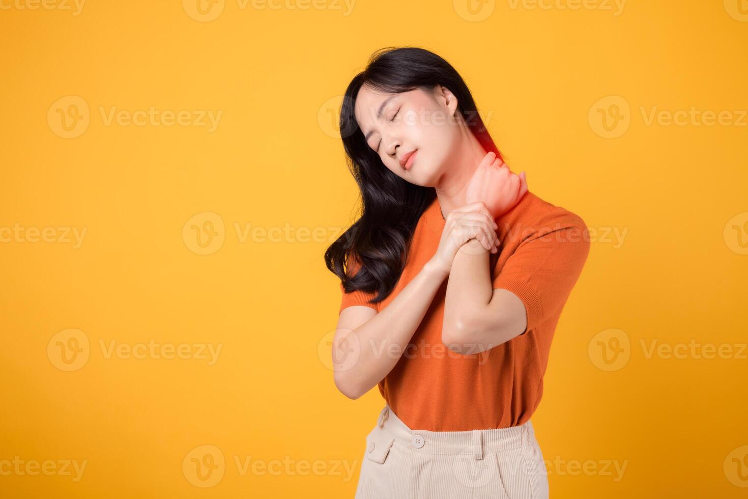 preocupado ásia mulher dentro dela 30s, vestindo a laranja camisa, detém dela doloroso pescoço em amarelo fundo. escritório síndrome saúde Cuidado conceito. foto