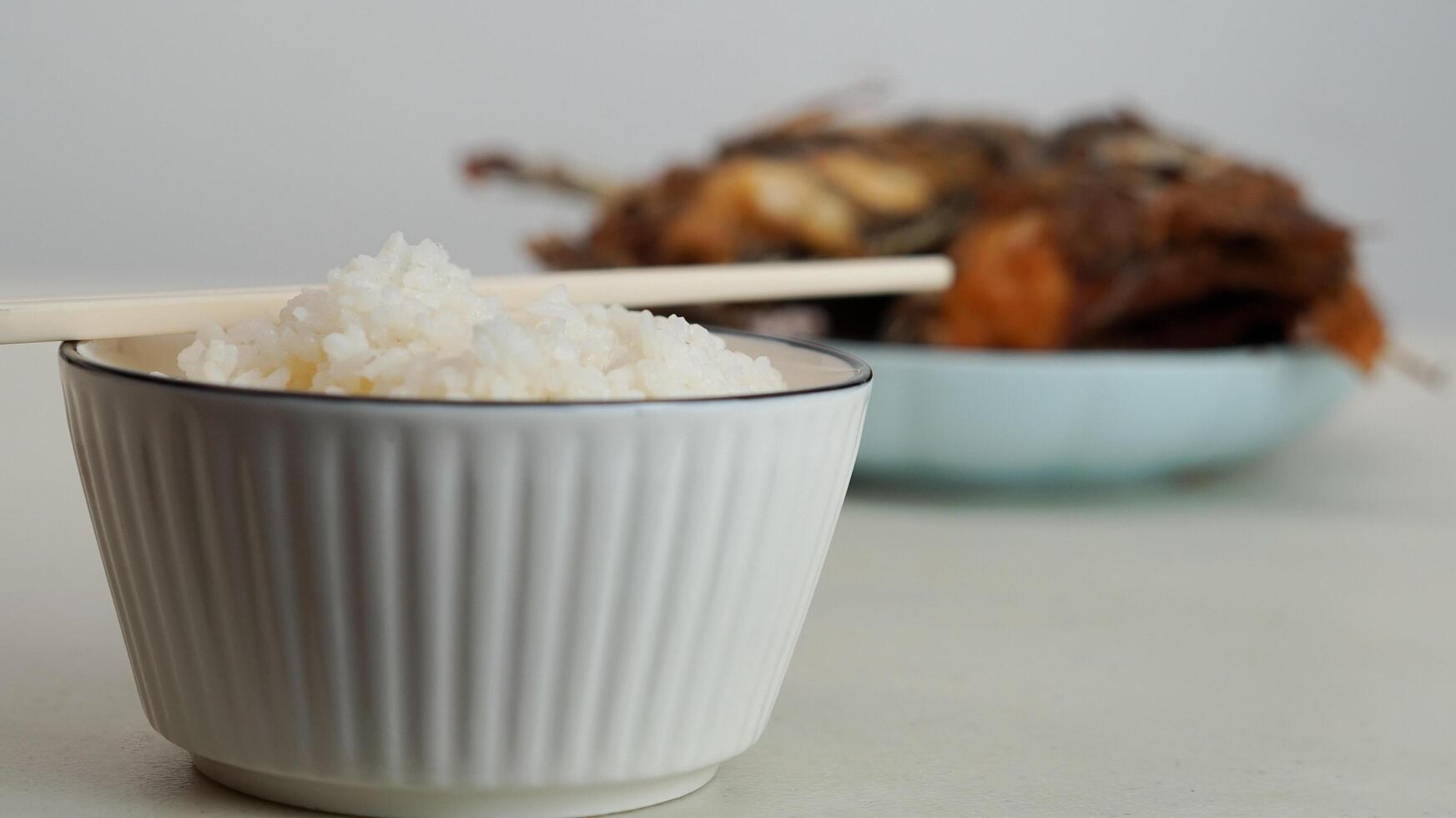 branco arroz dentro uma tigela e frito peixe em uma branco prato estão servido em a mesa foto