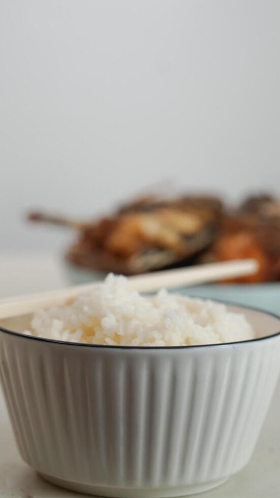 branco arroz dentro uma tigela e frito peixe em uma branco prato estão servido em a mesa foto