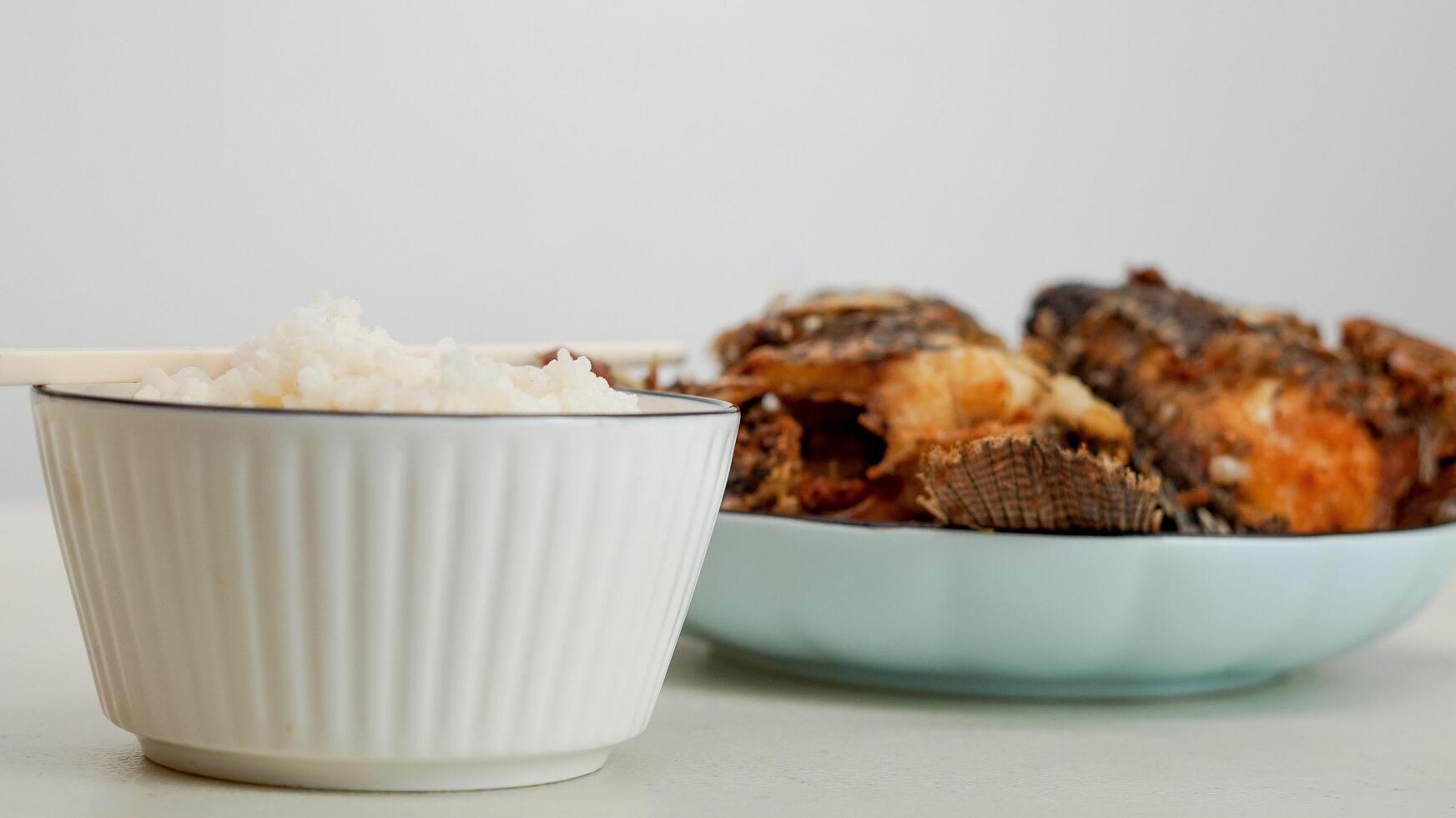 branco arroz dentro uma tigela e frito peixe em uma branco prato estão servido em a mesa foto