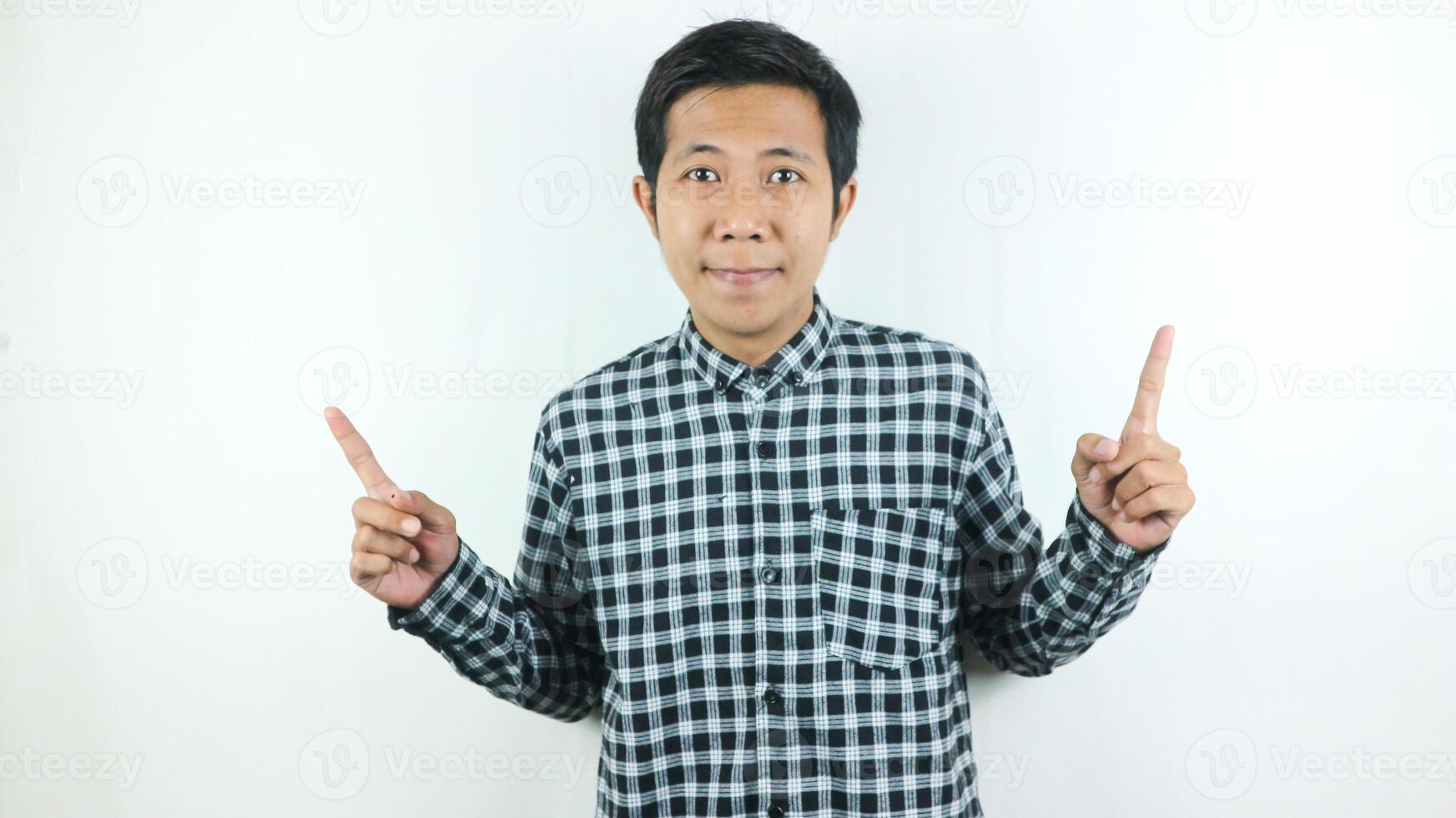 adulto ásia homem vestindo xadrez camisa sorridente enquanto olhando e apontando acima lado. foto