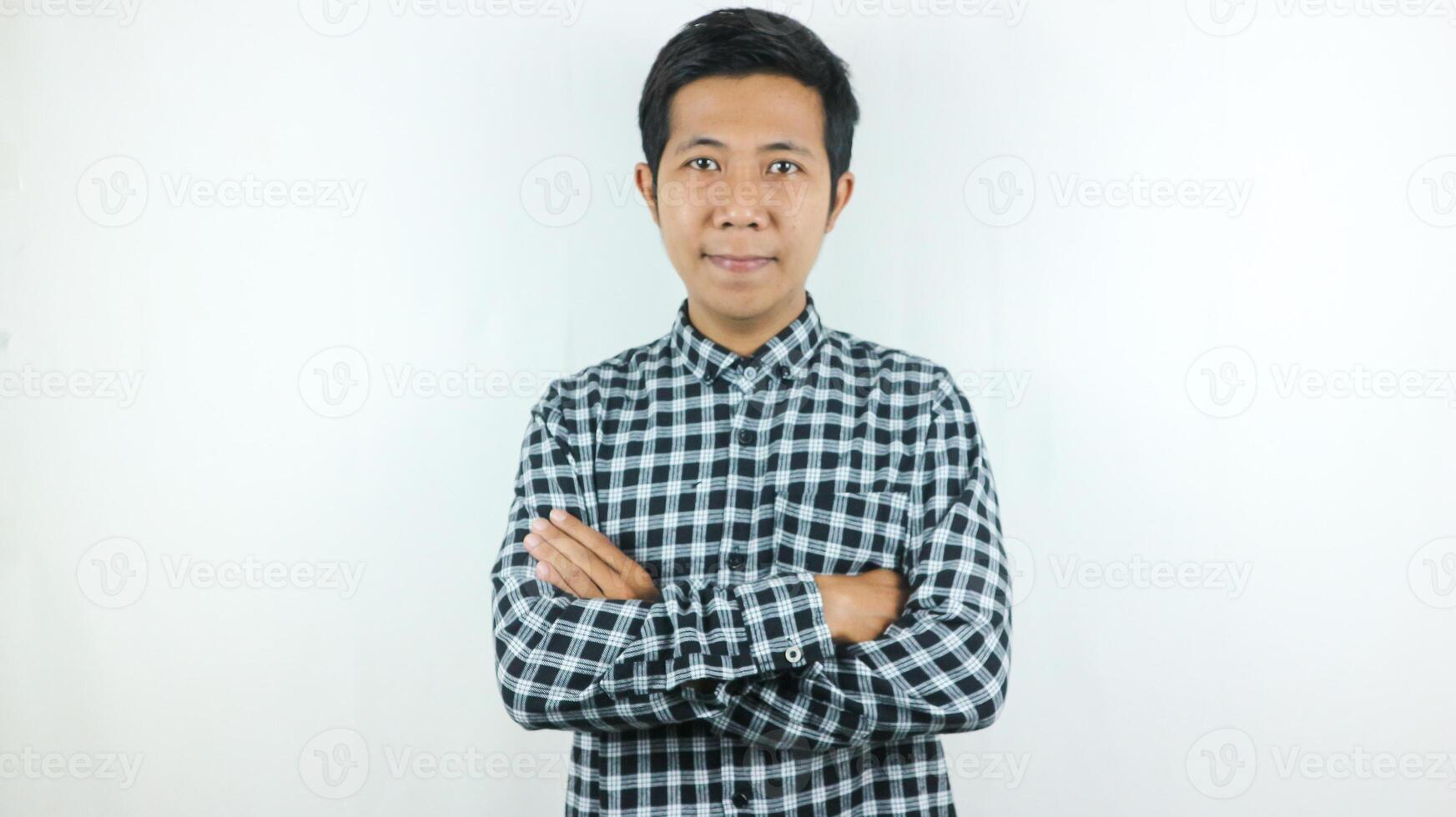 sorridente ásia homem vestindo xadrez camisa com cruzado braços olhando às Câmera estúdio tiro isolado em branco fundo. foto