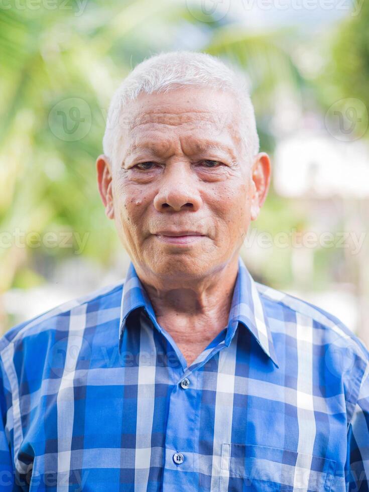 Senior homem desgasta uma azul camisa ficar de pé dentro jardim foto