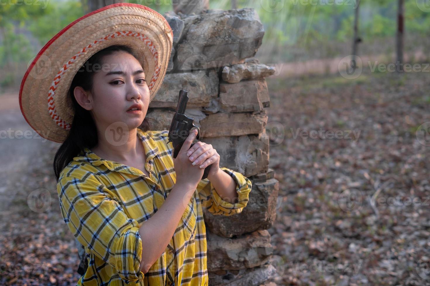 retrato do agricultor asea mulher vestindo uma camisa amarela segurando uma velha arma de revólver na fazenda, jovem com uma arma no jardim foto