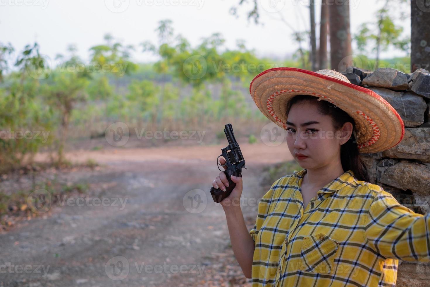 retrato do agricultor asea mulher vestindo uma camisa amarela segurando uma velha arma de revólver na fazenda, jovem com uma arma no jardim foto