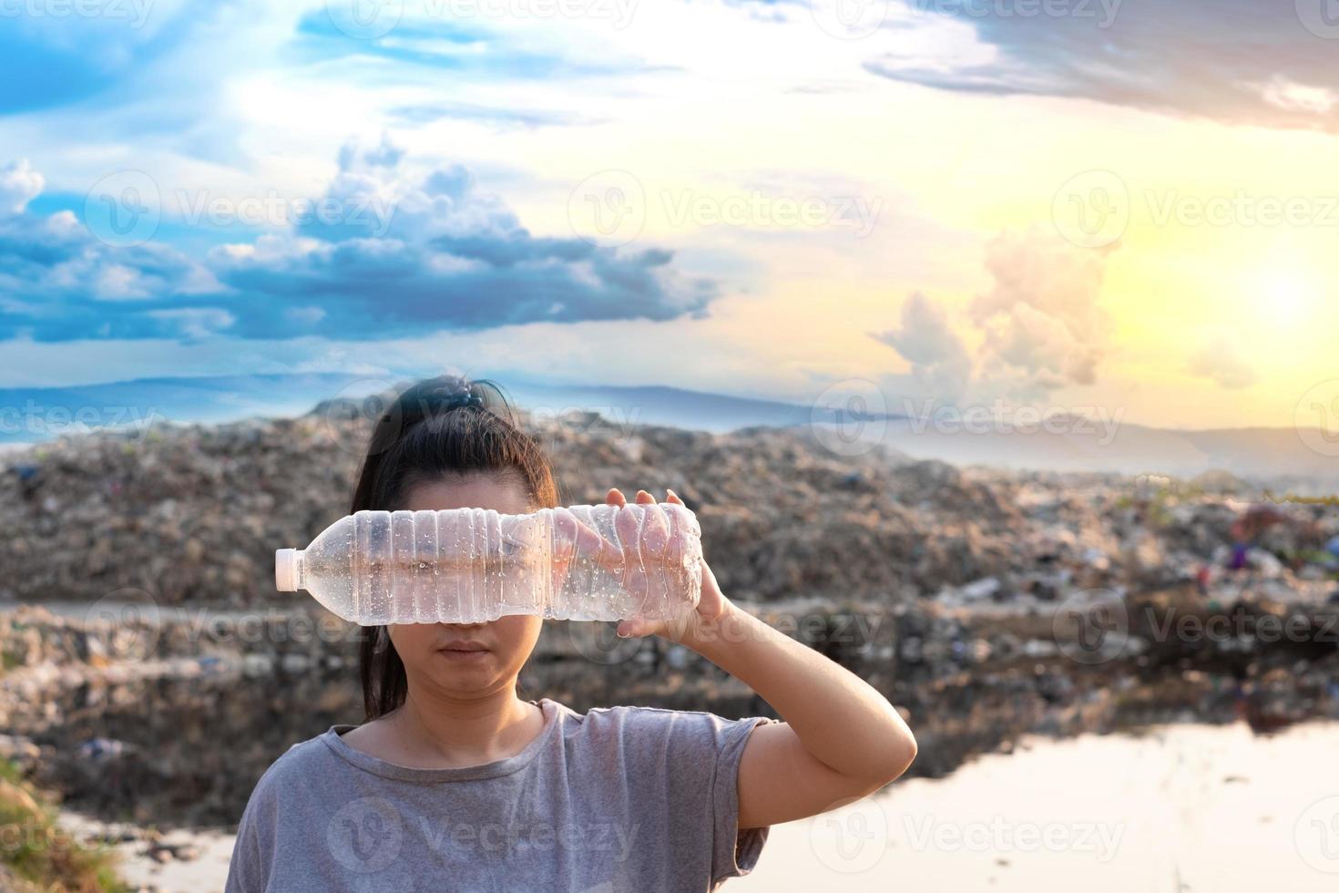 mão de uma mulher entregando uma garrafa de plástico transparente em uma montanha grande fundo de lixo foto