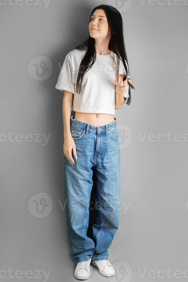 cheio comprimento retrato do uma jovem menina dentro uma branco camiseta e jeans. foto
