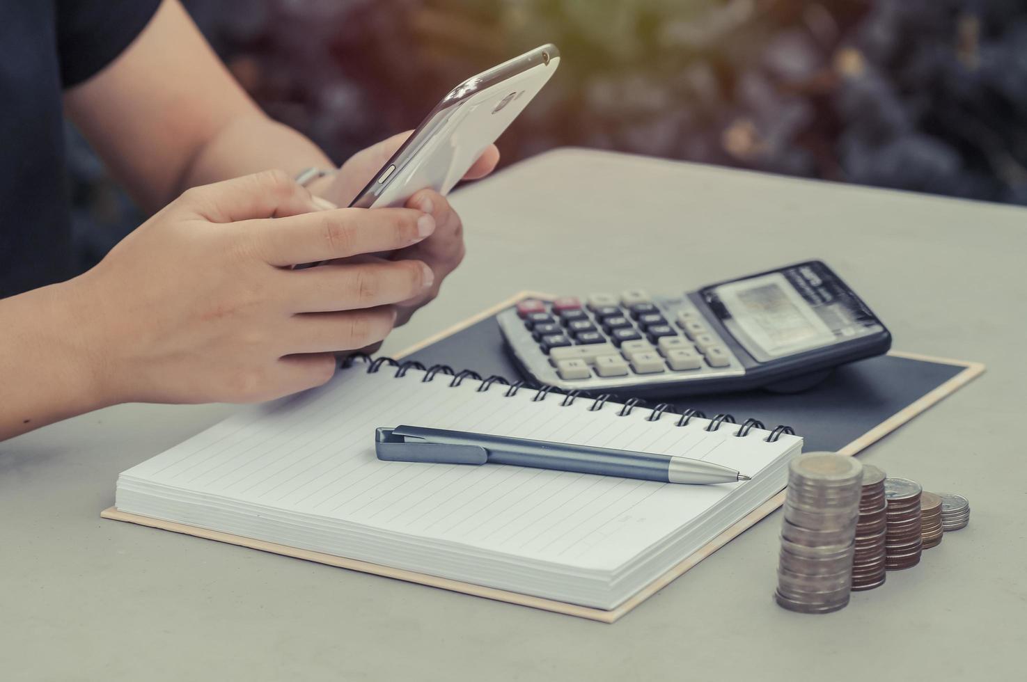 mulheres usam telefone com livro, calculadora e moedas na mesa foto