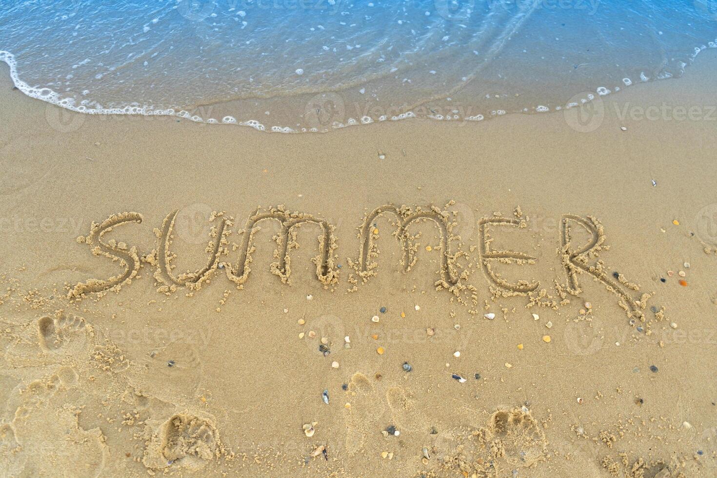 a palavra verão é escrito em a amarelo areia do a de praia. azul onda e surf. recorrer e período de férias. verão em a à beira-mar. relaxamento descansar conceito foto