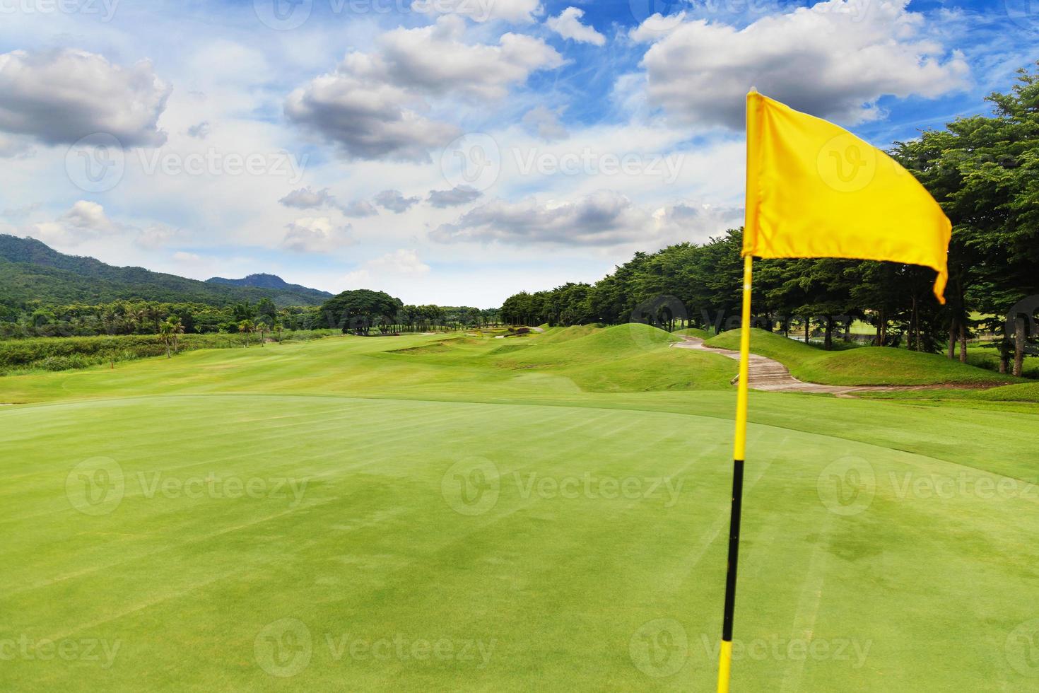 bandeira amarela no lindo campo de golfe com céu azul foto