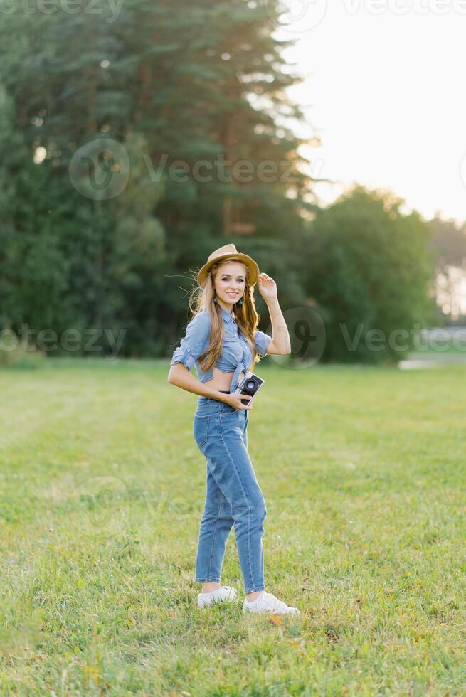 atraente jovem mulher com uma Câmera dentro dela mãos é em repouso e levando As fotos ao ar livre