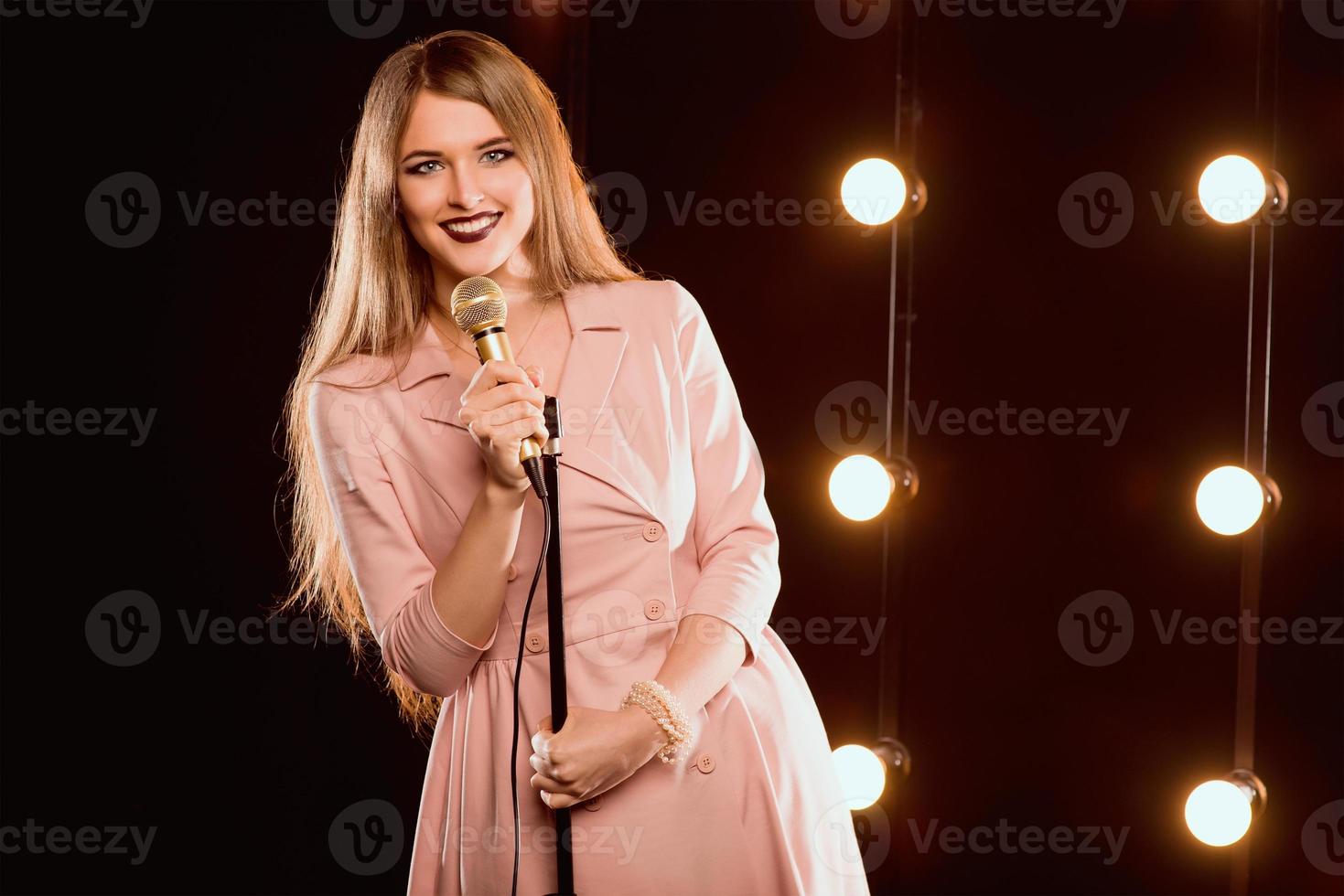 Jovem sorridente linda garota de cabelo comprido com microfone cantando no palco no karaokê foto