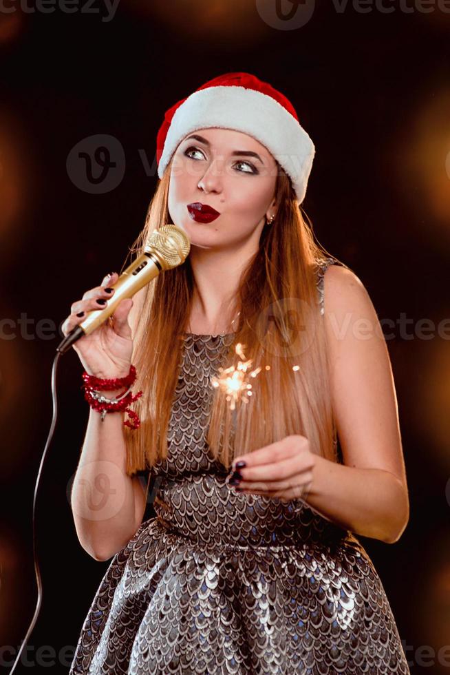 jovem loira atraente com chapéu vermelho de ano novo com microfone e diamante cantando no palco foto