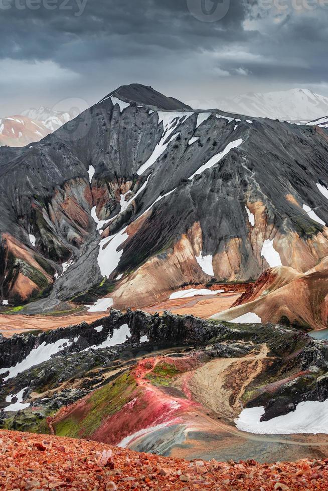 incrível paisagem islandesa de montanhas vulcânicas de arco-íris coloridas landmannalaugar, na famosa trilha de caminhada laugavegur com céu nevado dramático e solo de vulcão vermelho na Islândia foto