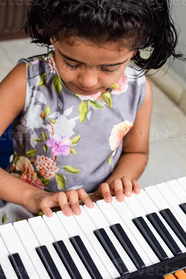 ásia fofa menina jogando a sintetizador ou piano. fofa pequeno criança Aprendendo quão para jogar piano. criança mãos em a teclado interior. foto