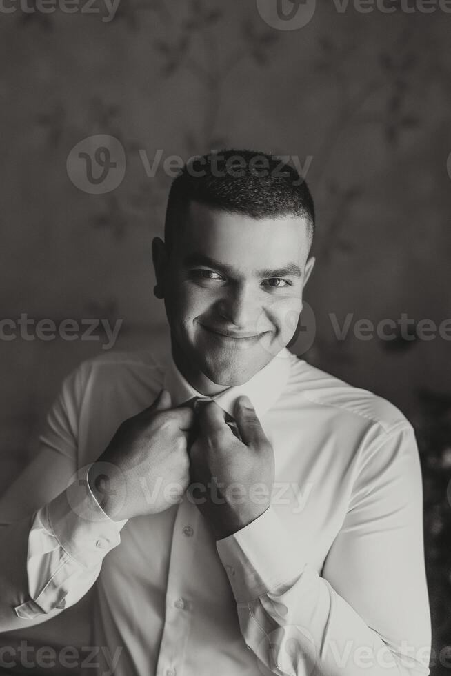 a noivo botões dele camisa de a janela. homem dentro uma camisa. masculino retrato. sessão de fotos às a janela. do noivo coleção. Casamento dia. bonito homem noivo abotoar dele camisa dentro uma hotel sala.