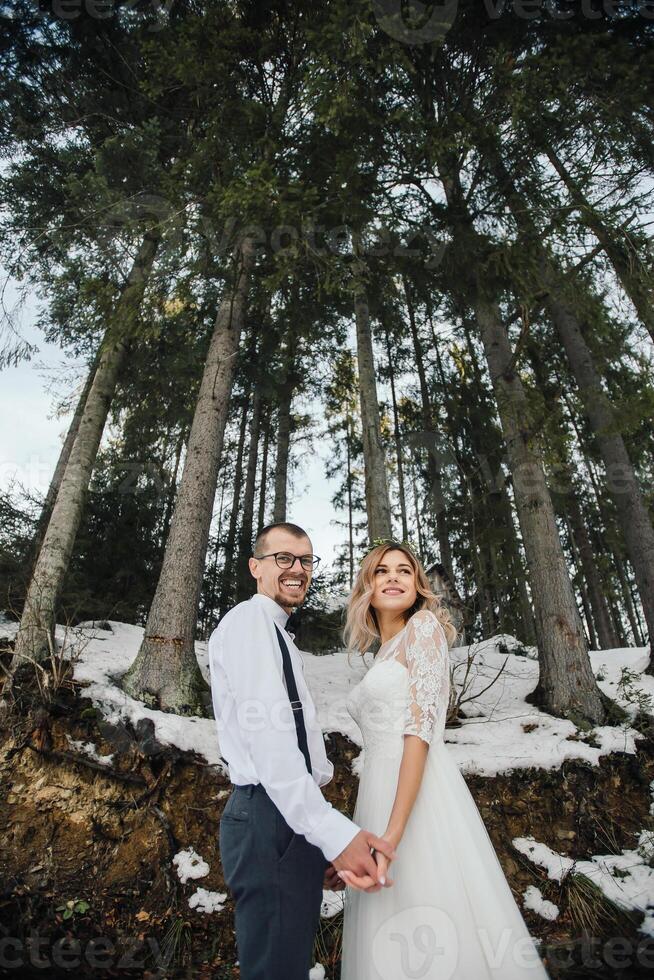 uma jovem casal, a noiva e noivo, sorrindo mostrar fora seus Casamento argolas contra a fundo do alta árvores ter uma Boa Tempo rindo. inverno Casamento foto