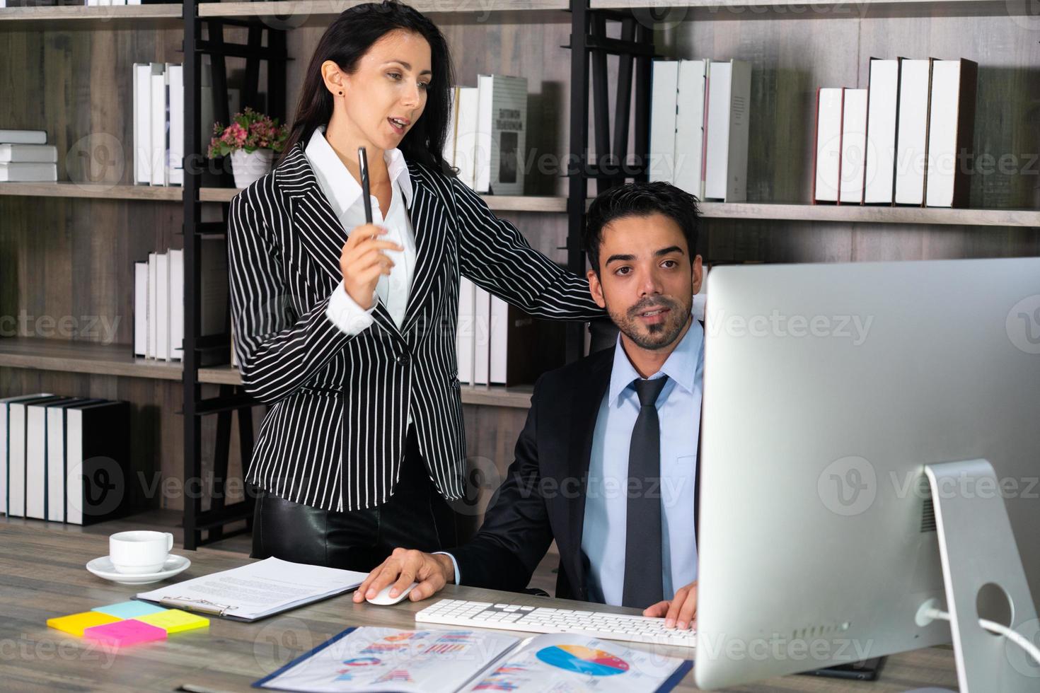 jovem empresário do Oriente Médio sentado na cadeira e empresária caucasiana em pé ao lado de seu colega no escritório. conceito de negócios foto