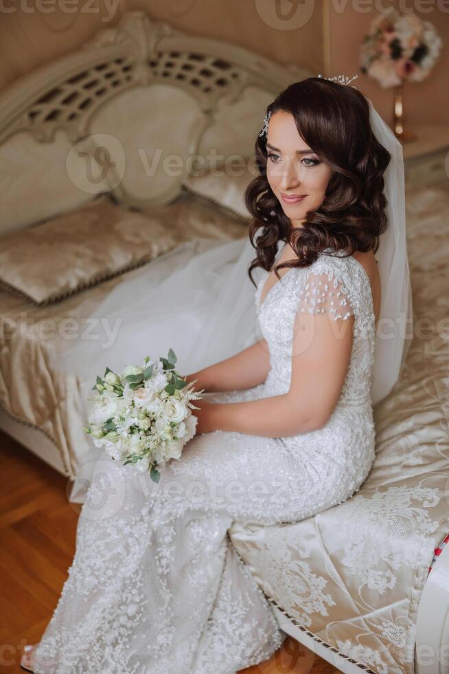 uma Maravilhoso lindo retrato do uma jovem noiva. lindo noiva com Casamento Maquiagem e joalheria guirlanda em grandes encaracolado cabelo. Casamento foto modelo com Castanho olhos dentro uma lindo interior.