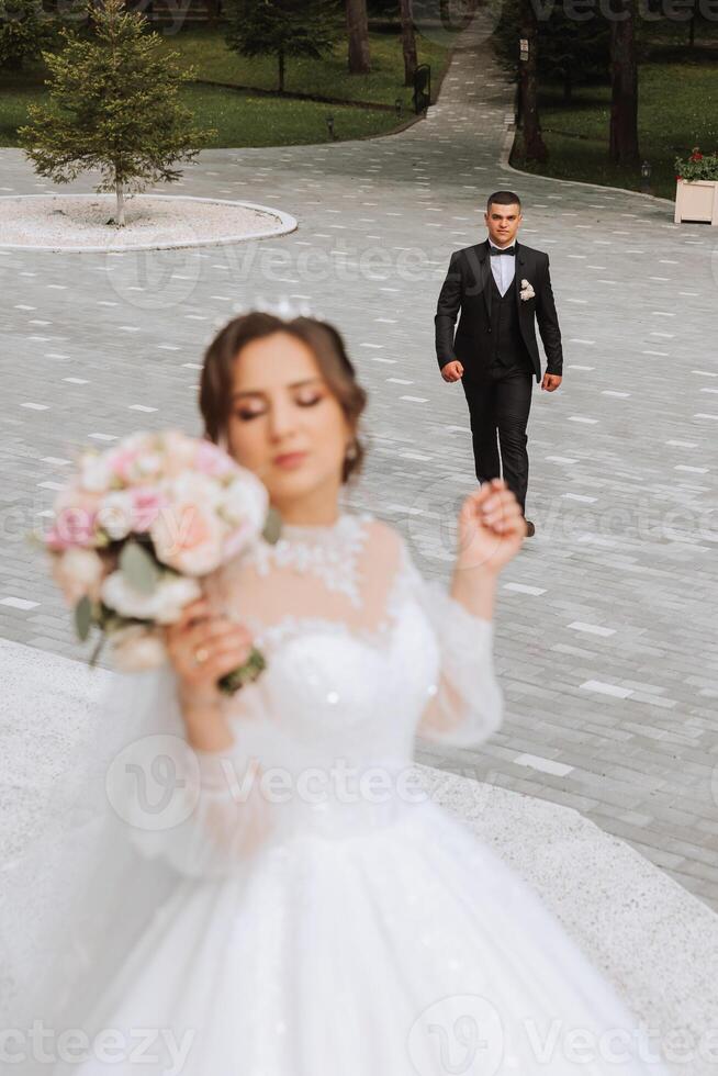 lindo jovem noiva dentro verão parque em pé dentro frente do dela noivo, foto com seletivo foco. lindo Casamento branco vestir. anda em dentro a parque. uma feliz e amoroso casal.