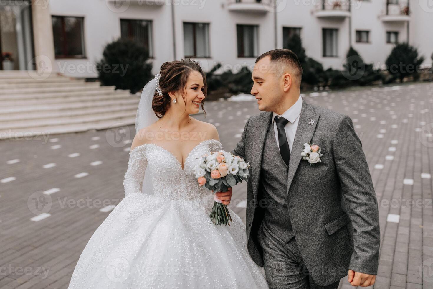 uma noiva dentro uma branco vestir com uma trem e uma noivo dentro uma terno pose em a passos do uma prédio. Casamento foto sessão dentro natureza