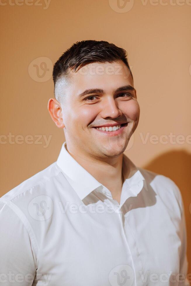 uma jovem sorridente homem dentro uma branco camisa é olhando às a Câmera. noivo com uma curto Penteado em a laranja fundo foto