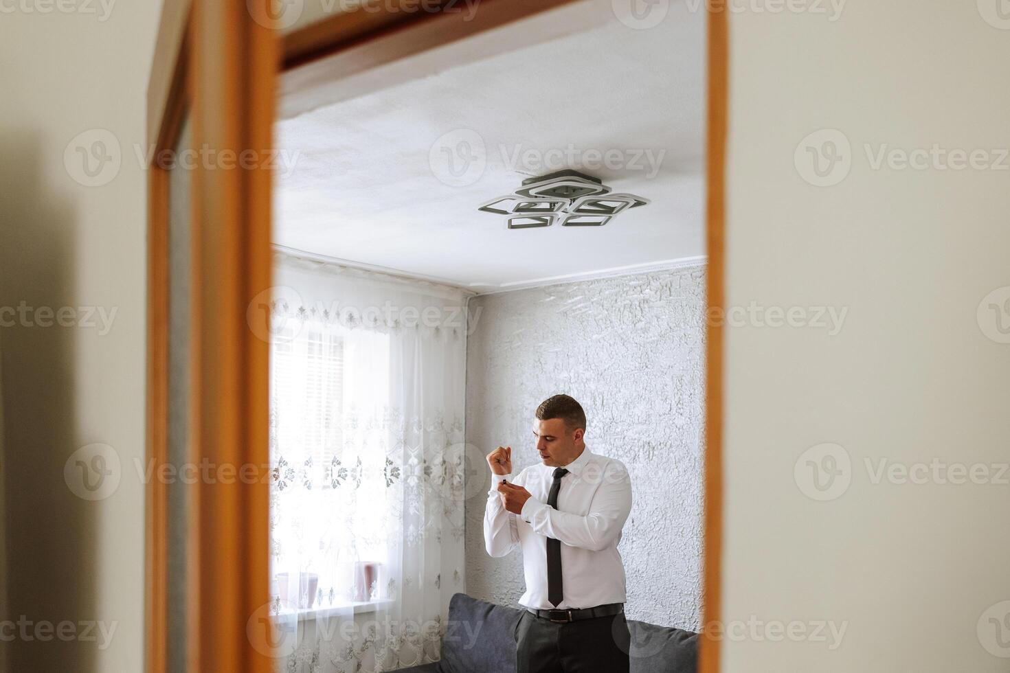 a noivo botões dele camisa de a janela. homem dentro uma camisa. masculino retrato. sessão de fotos às a janela. do noivo coleção. Casamento dia. bonito homem noivo abotoar dele camisa dentro uma hotel sala.