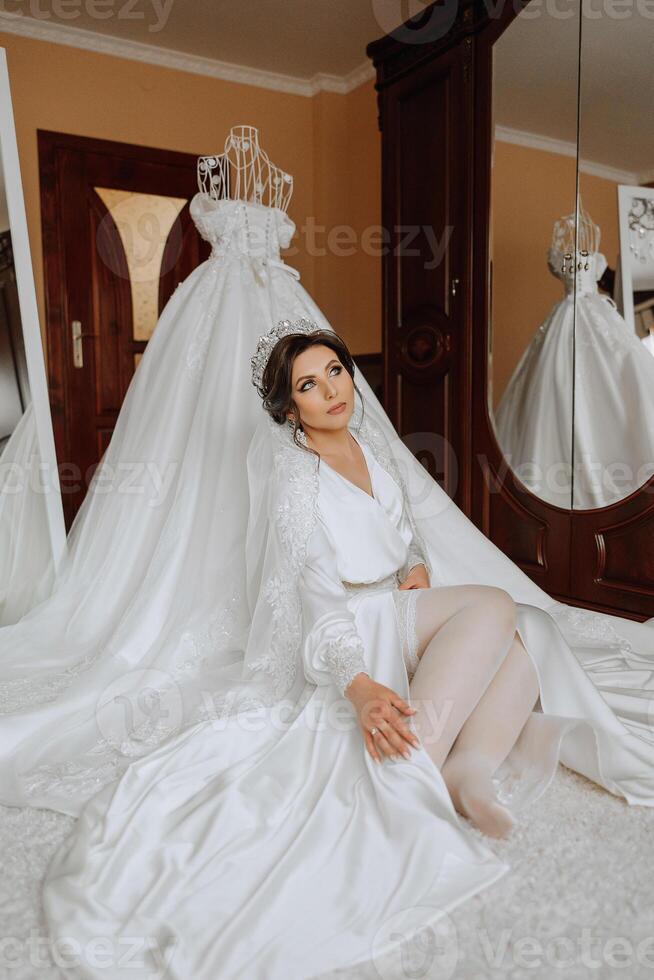 uma lindo morena noiva com uma tiara dentro dela cabelo é obtendo pronto para a Casamento dentro uma lindo roupão dentro boudoir estilo. fechar-se Casamento retrato, foto. foto