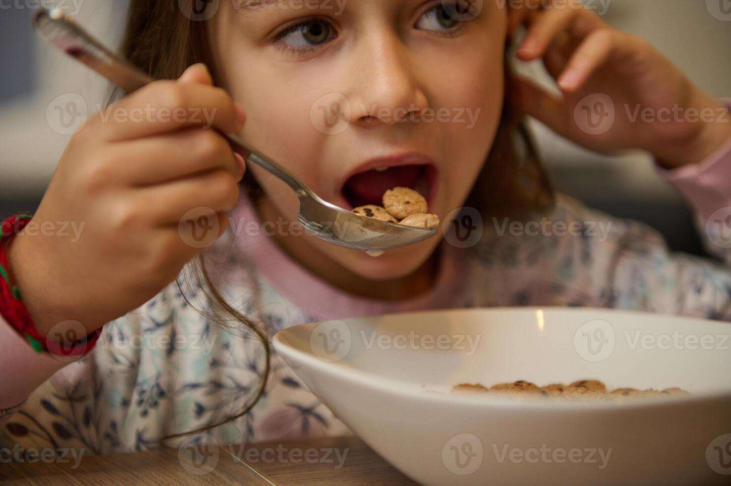 fechar-se face retrato do com fome criança menina segurando cheio mesa colher do doce delicioso milho aveia flocos com leite querida foto