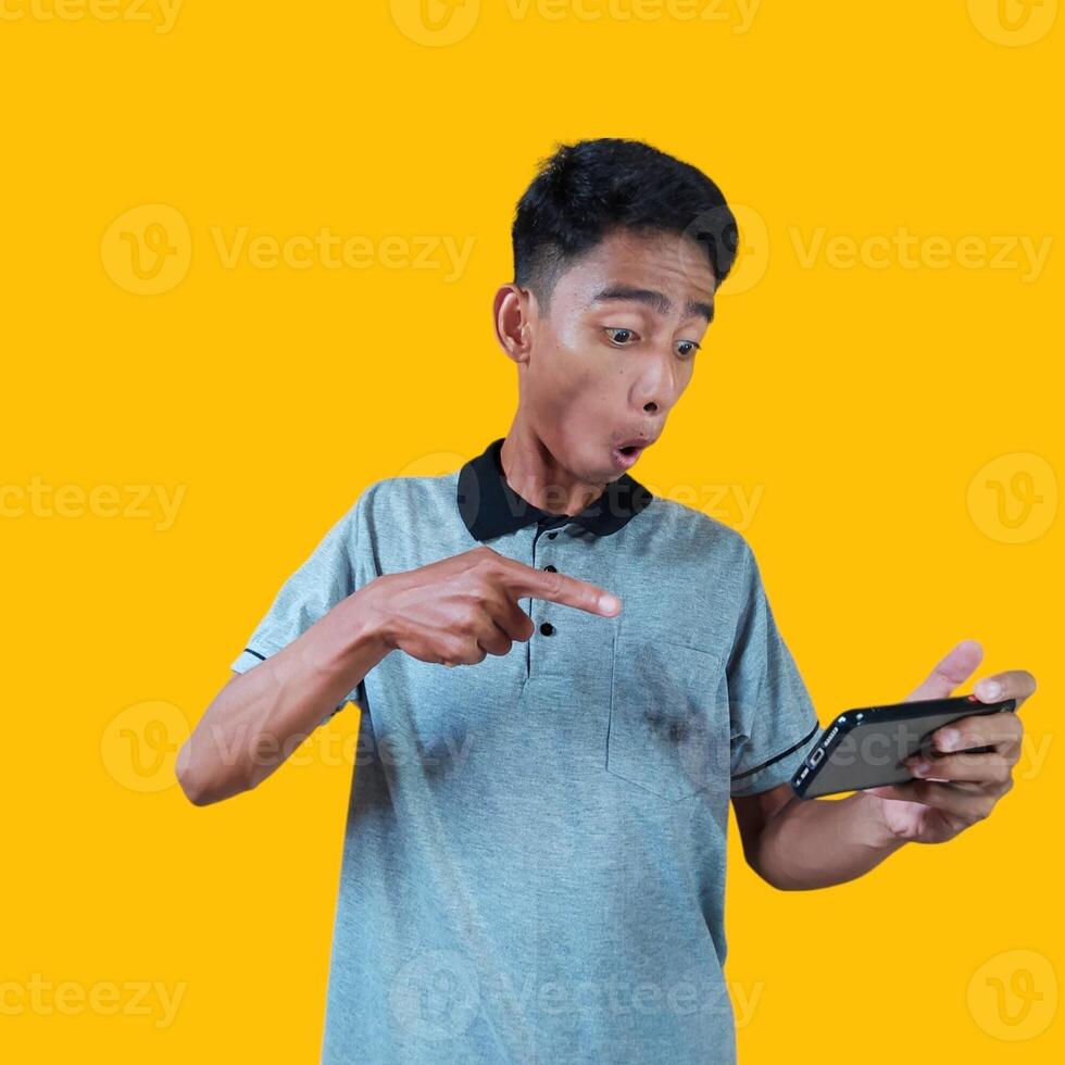 animado jovem homem segurando uma inteligente telefone vestindo uma cinzento camiseta, amarelo fundo. foto