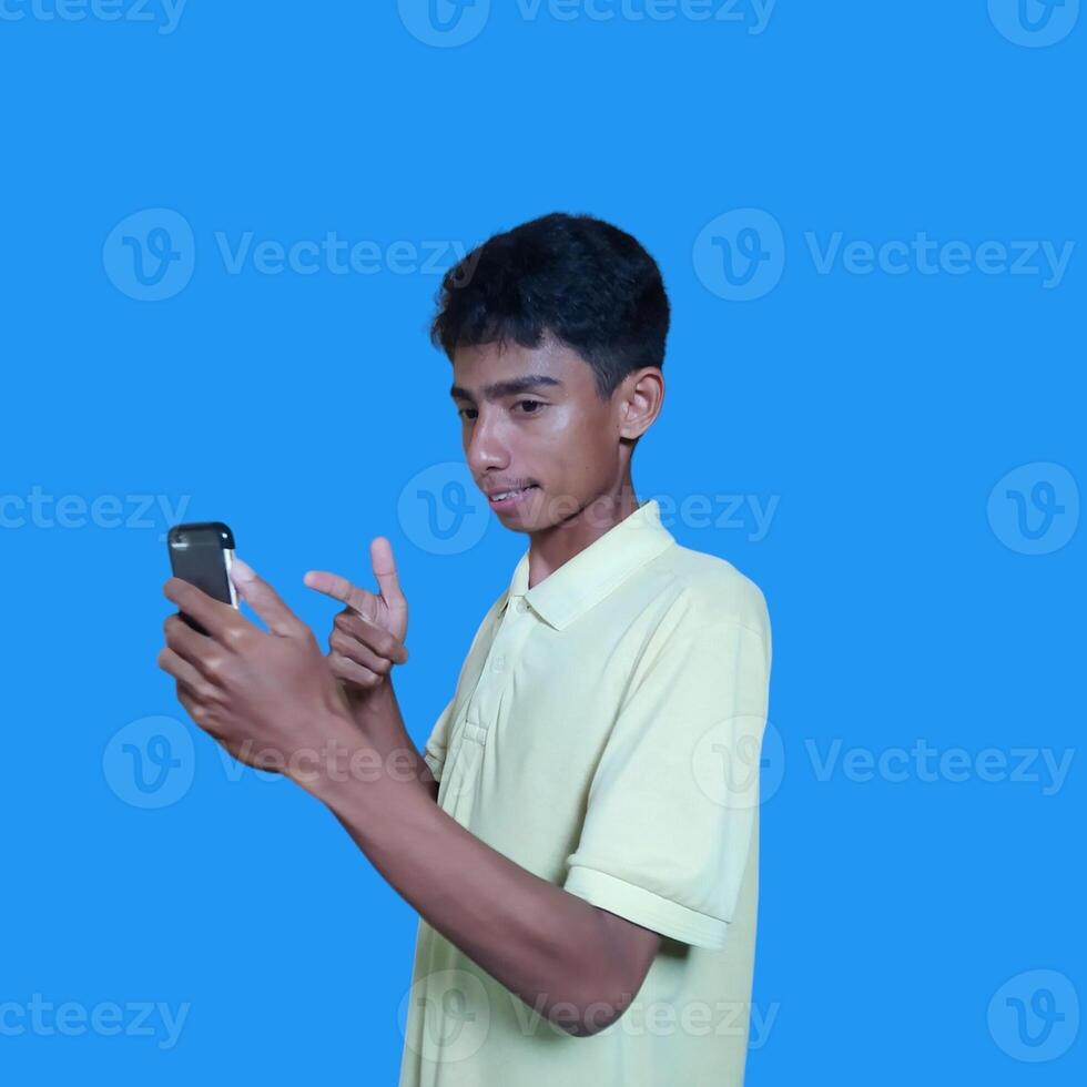 jovem ásia homem surpreso olhando às inteligente telefone isolado azul fundo foto